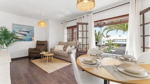 A modern living room with a sofa, a dining table set for two, and a painting of boats on the wall.