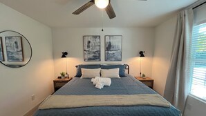 Een slaapkamer met een bed, twee nachtkastjes, een plafondventilator en twee wandlampen.