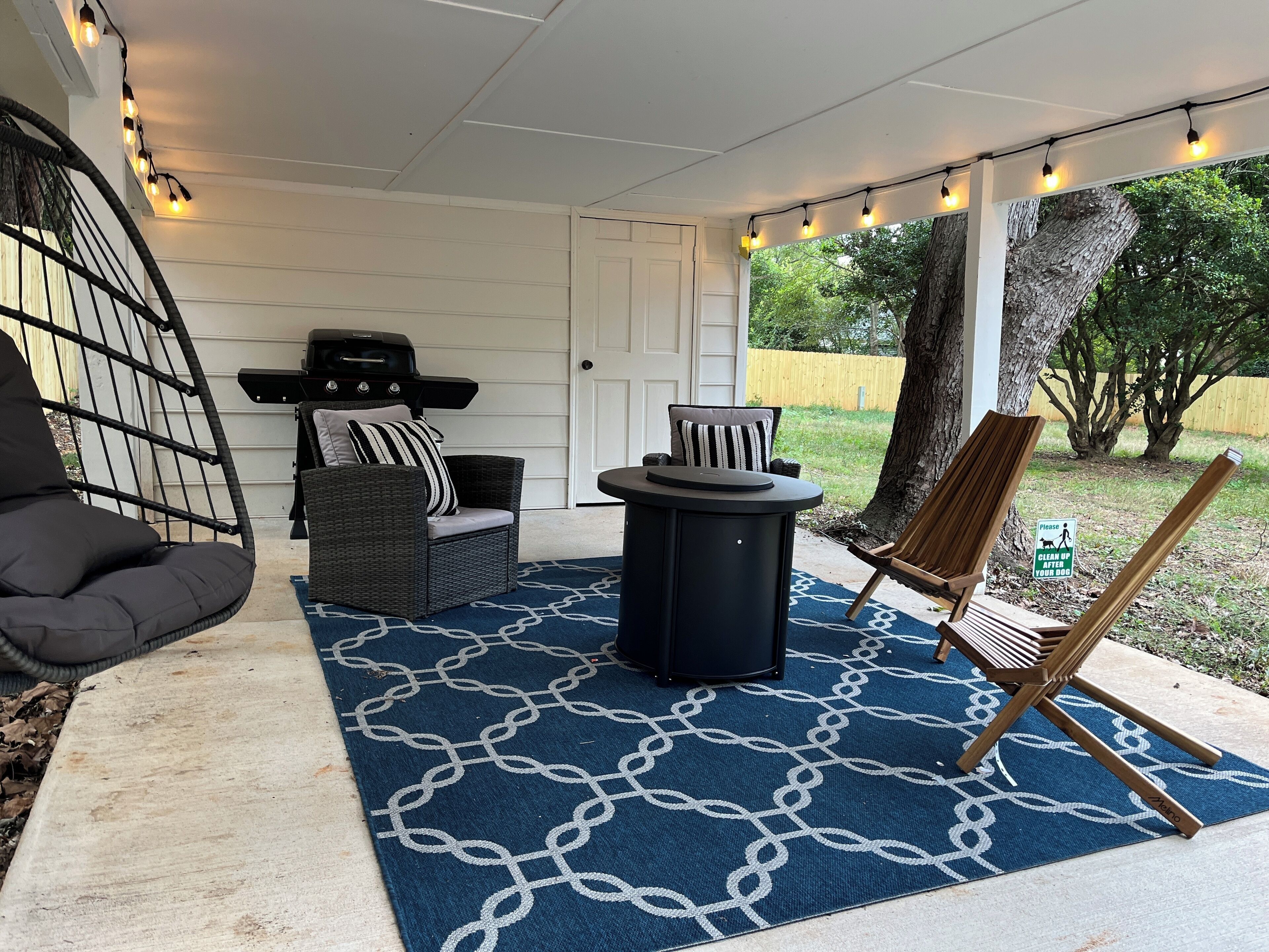 Un patio couvert aménagé avec du mobilier d’extérieur, des guirlandes lumineuses et un tapis à motifs bleus.
