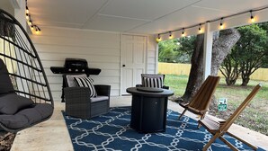 Een overdekt terras met buitenmeubilair, lichtslingers en een blauw gekleurd vloerkleed.
