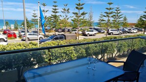 A balcony with a table and chairs, overlooking a parking area with cars and a flag. - Scarborough Shores - Beachfront (Scarborough)