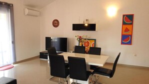 A dining area with a white table, black chairs, a TV, and a clock on the wall. - Expansive Ciovo Apartment with Sea-Views, Balcony and Outdoor Dining - Three Bedroom Apartment (Okrug Gornji)