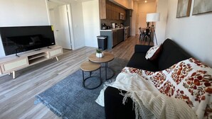 Ett modernt vardagsrum med en platt-TV, en soffa, ett soffbord och en matplats med stolar.
