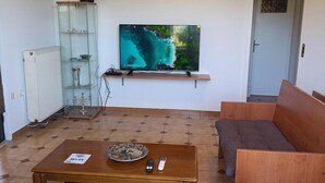 A living room with a television, a sofa, a coffee table, and a wooden bench. - Anatolis Apartment: Near Airport, Rafina Port & Beach (Artemis)