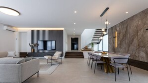 Un salon moderne comprenant un canapé, un coin repas avec des chaises et une table, un escalier et un téléviseur fixé au mur.