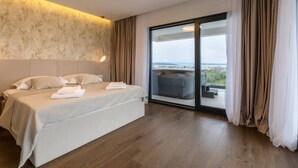 Une chambre d’hôtel moderne avec un grand lit, une vue sur la mer et une porte-fenêtre coulissante donnant sur le balcon.