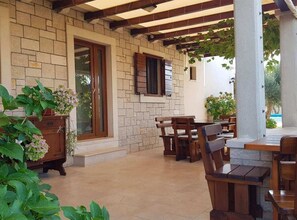 An outdoor patio area with stone walls, wooden furniture, and potted plants. - Secluded Oasis with Pool, Outdoor Kitchen, & Landscaped Terraces - Three Bedroom Villa (Supetar)
