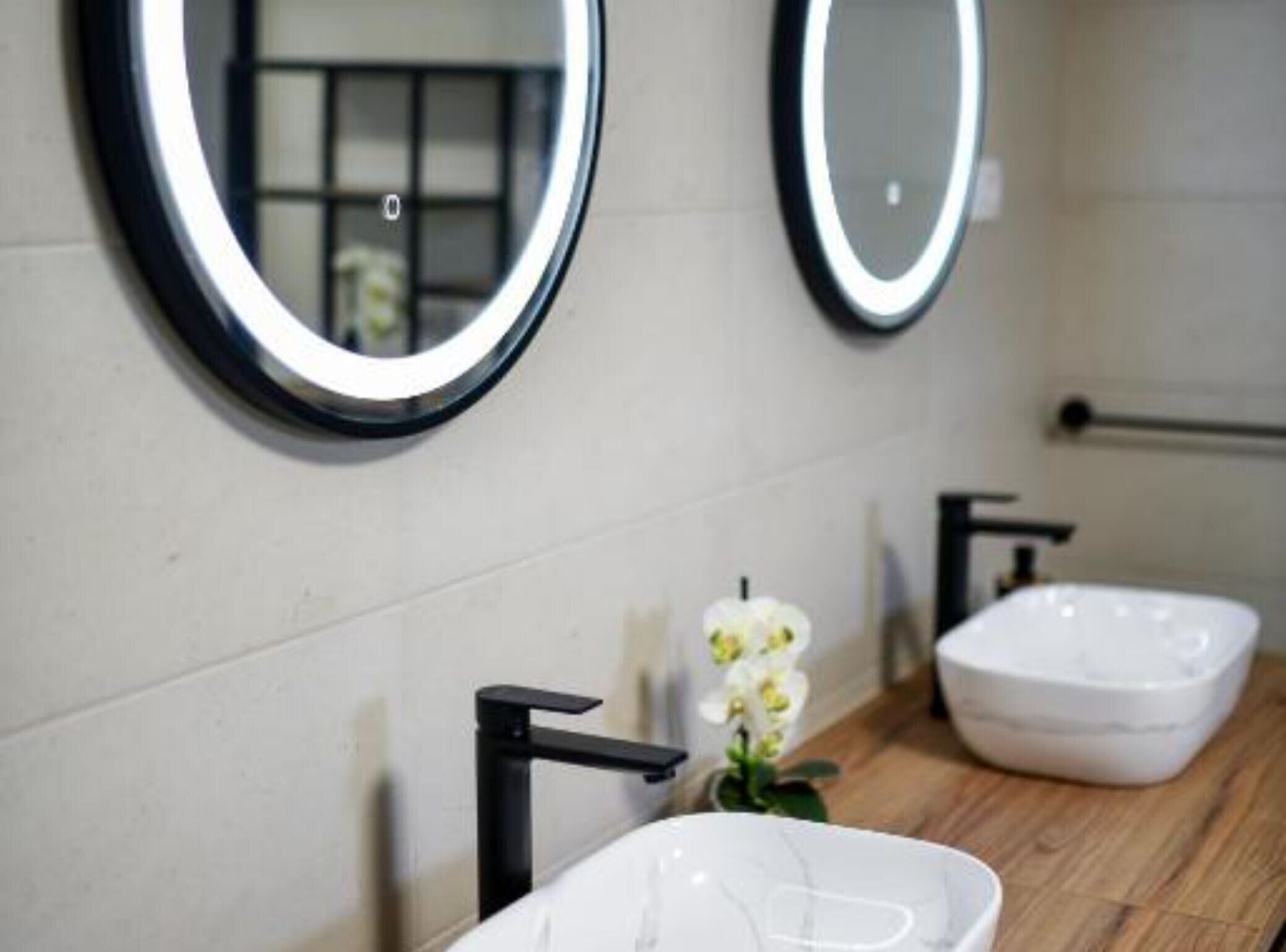 Ein Badezimmer mit zwei runden Spiegeln, einem weißen Waschbecken und einem schwarzen Wasserhahn.