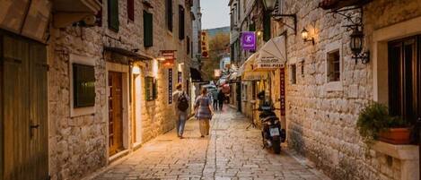 A narrow cobblestone street lined with stone buildings, some with signs for businesses like a grill-pizza restaurant.