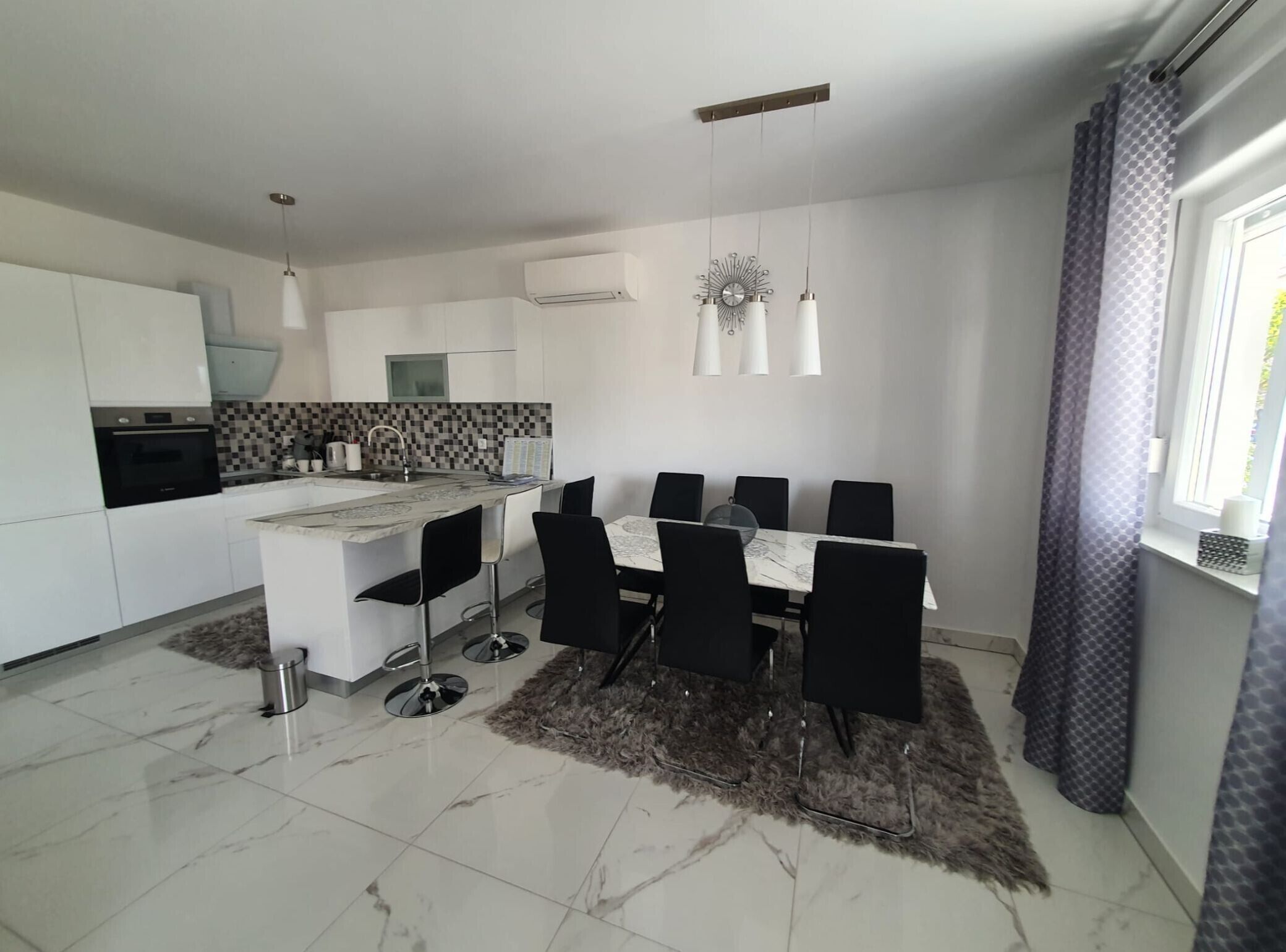A modern kitchen with a central island, black chairs, and a dining table.