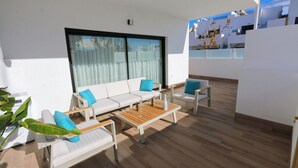 A modern outdoor living area with a white sofa, two armchairs, and a wooden table.