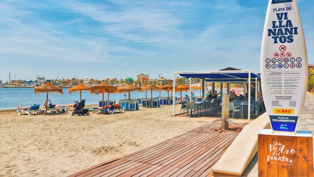 A beach with sun loungers, umbrellas, and a wooden boardwalk.