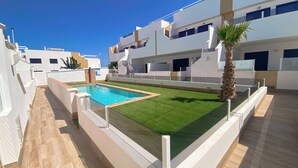 A modern apartment complex with a swimming pool, artificial grass, and a palm tree.