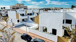 A modern residential area with white buildings, a clear sky, and a few cars parked on the street.