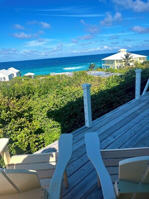 A wooden deck with chairs overlooking a coastal view, including a beach and ocean. - Love Shack Ocean View bungalow.  (Hope Town)