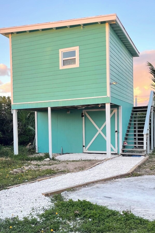 Un edificio de dos pisos con fachada verde y una ventana pequeña en el nivel superior.