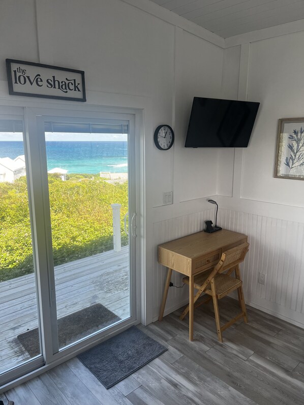 Een kamer met uitzicht op de oceaan, een houten bureau, een aan de muur bevestigde televisie en een bordje met de tekst 'the love shack'.