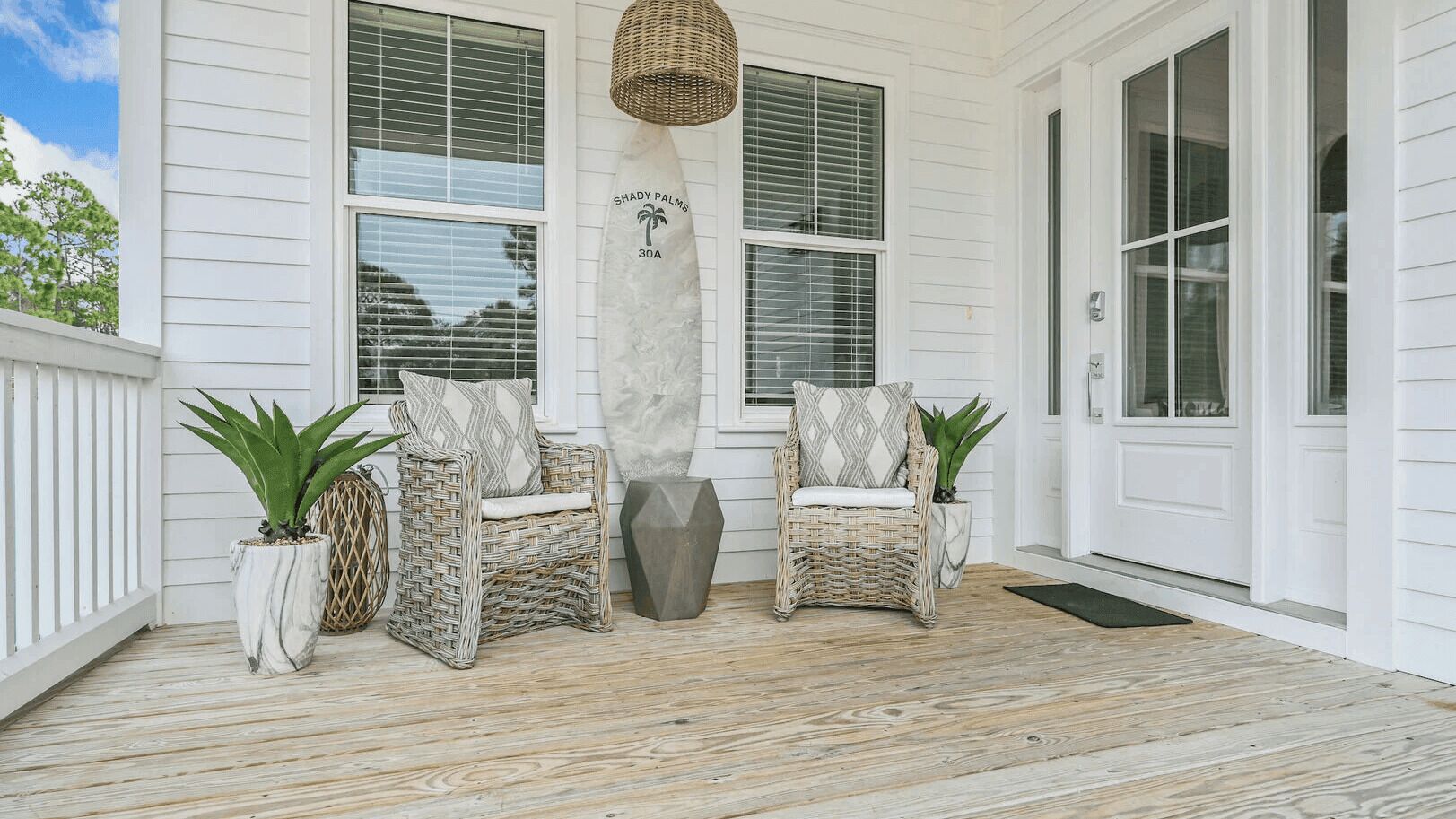 A porch with two wicker chairs, a potted plant, and a decorative wall hanging.