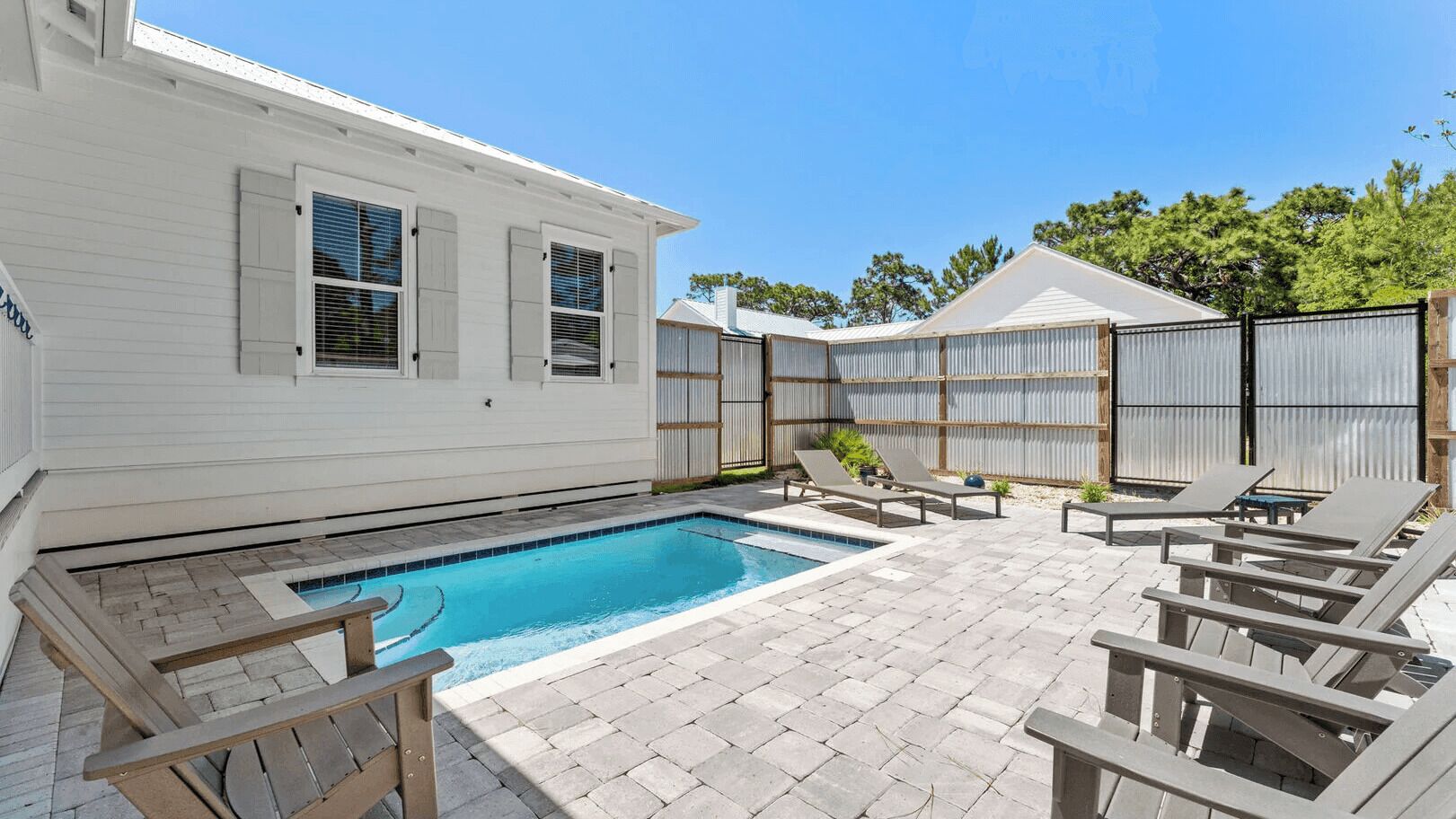 A swimming pool with lounge chairs and a covered area, surrounded by a fenced yard.