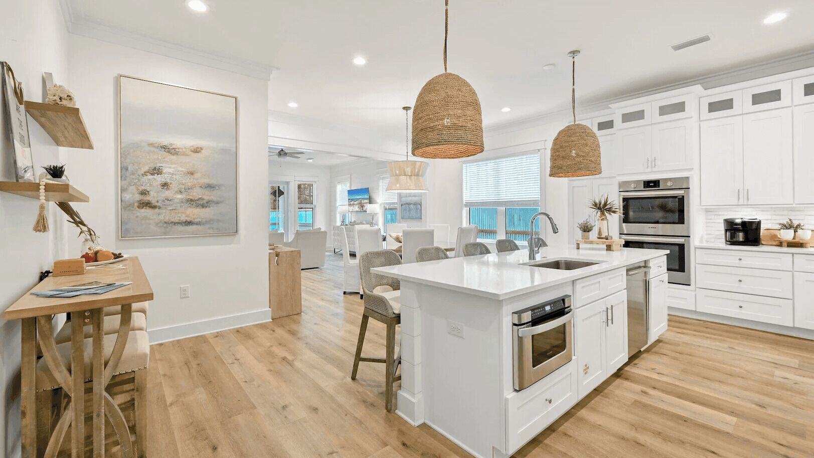 A modern kitchen with white cabinetry, a central island, stainless steel appliances, and woven pendant lights.