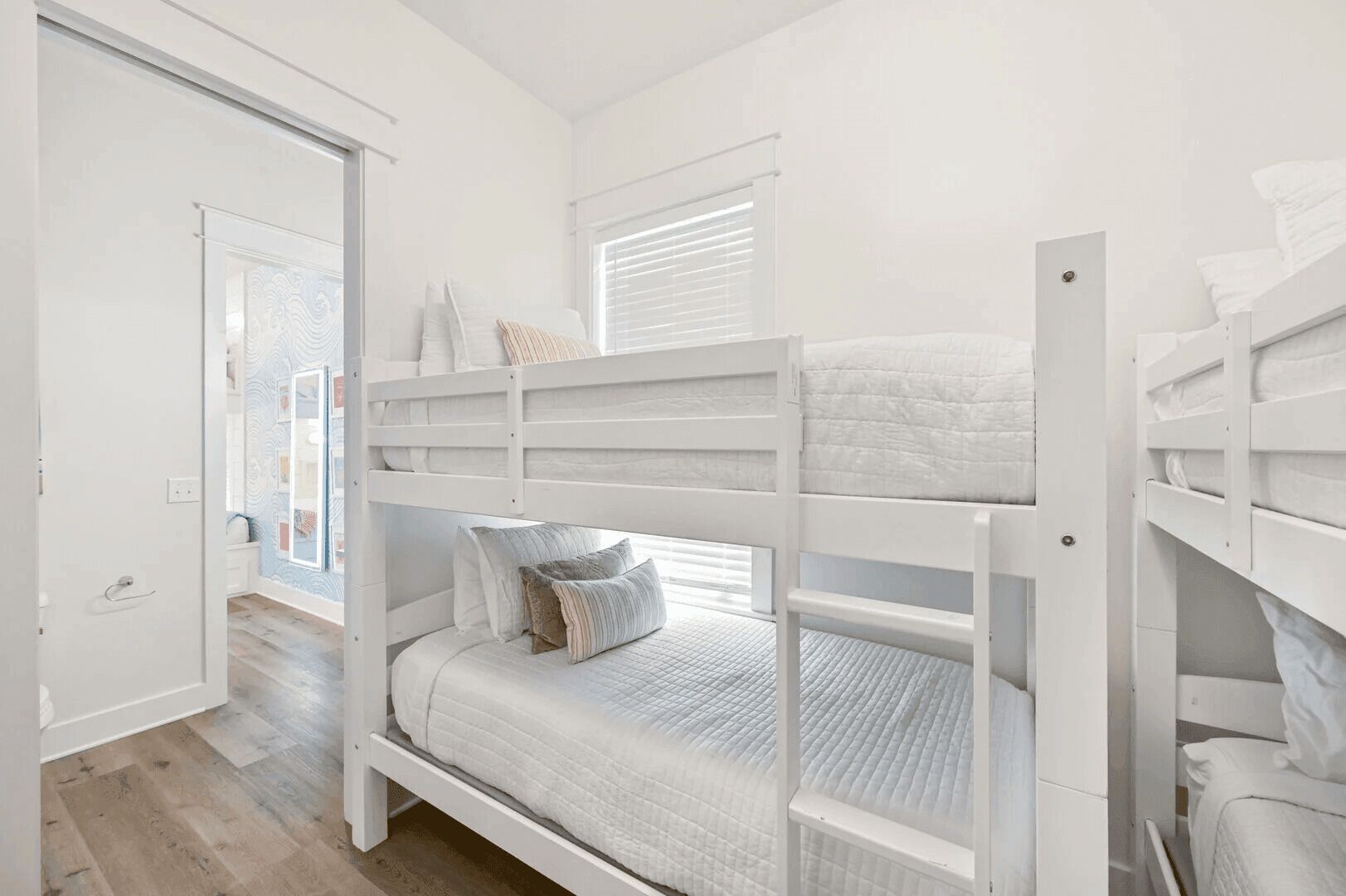 A bunk bed room with white bedding and a door leading to another room.