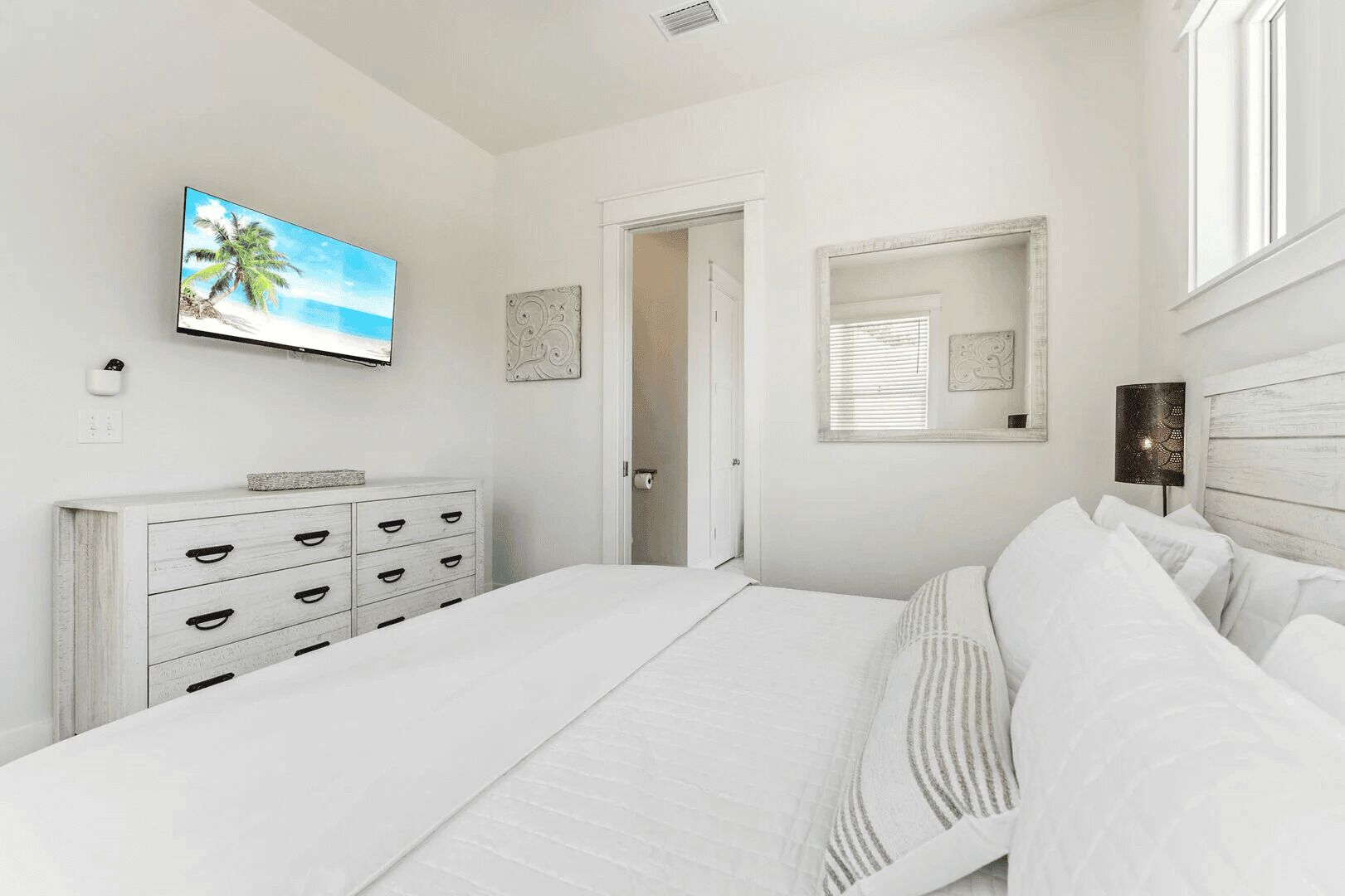 A bedroom with a bed, a dresser, a television, and a mirror.