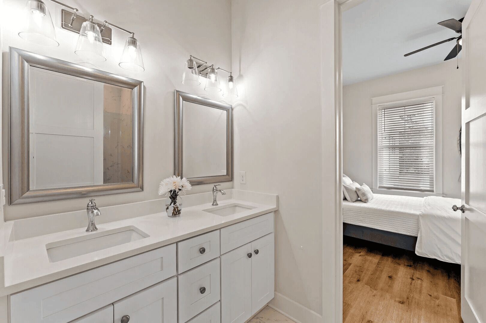 A bathroom with a double vanity, two large mirrors, a sink, and a vase with flowers.