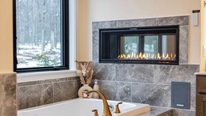 A modern bathroom with a freestanding bathtub, a built-in fireplace, and a window with a view of a snowy forest. - The Perfect Pocono Escape (coolbaugh township)