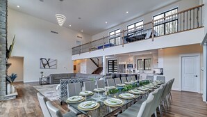 A spacious dining area with a long table set for a meal, a staircase leading to an upper level, and a kitchen in the background. - The Perfect Pocono Escape (coolbaugh township)