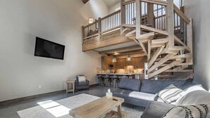 A spacious living area with a large sofa, a coffee table, and a staircase leading to an upper level. - Glacier Getaway •Hot Tub •King Beds  •Near Glacier (Coram)