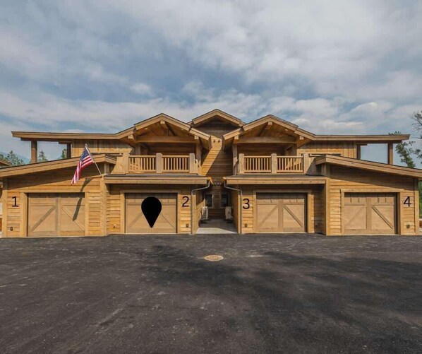Un ampio edificio in legno a più piani, con quattro porte per garage numerate da 1 a 4 e un ingresso centrale.