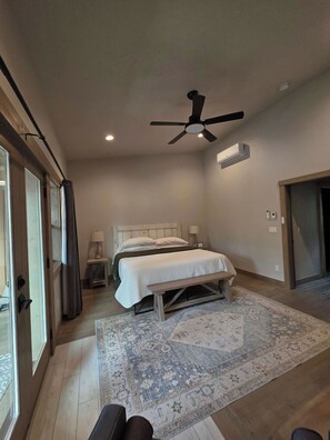 Un dormitorio con dos camas, ventilador de techo, unidad de aire acondicionado, un banco y una alfombra estampada.