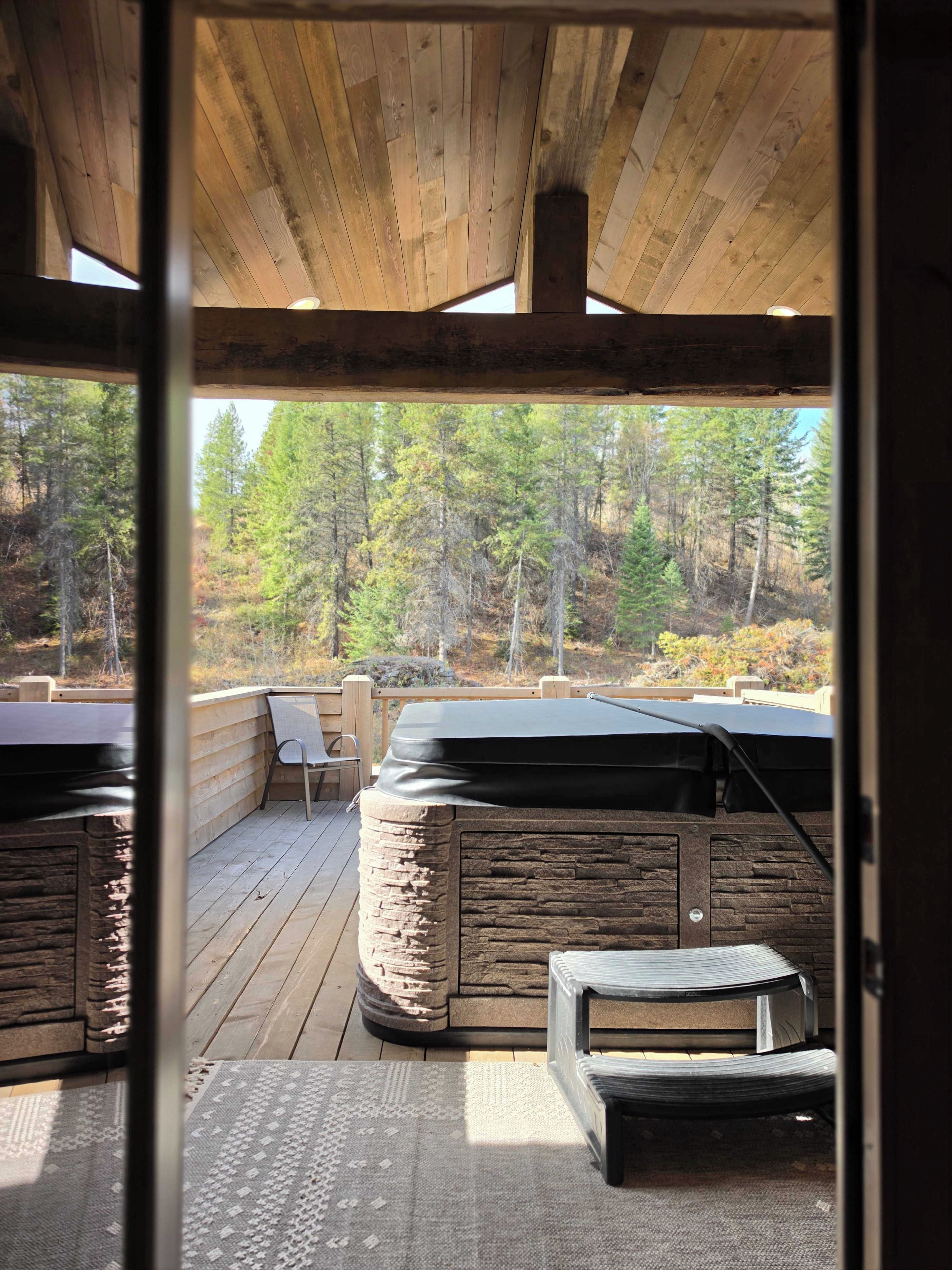 A wooden deck with a stone barbecue, outdoor seating, and a view of a forest.