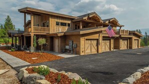 A large, two-story wooden house with a covered porch, multiple garage doors, and an American flag. - Glacier Getaway •Hot Tub •King Beds  •Near Glacier (Coram)