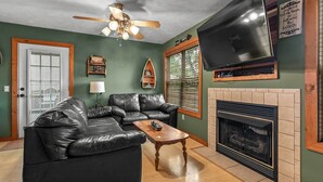 Ein Wohnzimmer mit Ecksofa, Couchtisch aus Holz, Kamin, Wand-Fernseher und Deckenventilator.