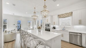 A modern kitchen with white cabinetry, a central island, and pendant lighting. - 30A Ocean Pearl by Avantstay Newly Built Pool Access + Golf Cart Walk to Dune Allen Beach (Santa Rosa Beach)