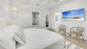 A bedroom with a bed, two wicker chairs, a ceiling fan, and a beach view painting. - 30A Ocean Pearl by Avantstay Newly Built Pool Access + Golf Cart Walk to Dune Allen Beach (Santa Rosa Beach)