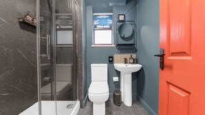 Ein Badezimmer mit einer gläsernen Duschkabine, einer weißen Toilette, einem Waschbecken und einer roten Tür.
