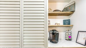 A kitchen with white cabinetry, a coffee maker, a decorative metal tray, and a framed menu on the countertop.