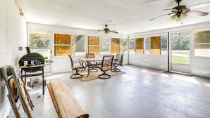 A sunlit room with a table and chairs, a ceiling fan, and large windows.