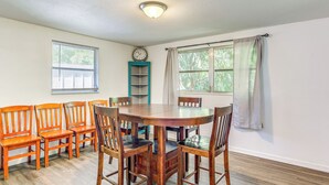 A dining area with a wooden table and chairs, a clock on the wall, and windows with curtains.