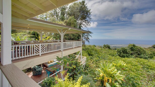A covered outdoor area with a wooden deck, seating, and lush greenery. - Lanai + Ocean Views: Secluded Holualoa Retreat! (Holualoa)