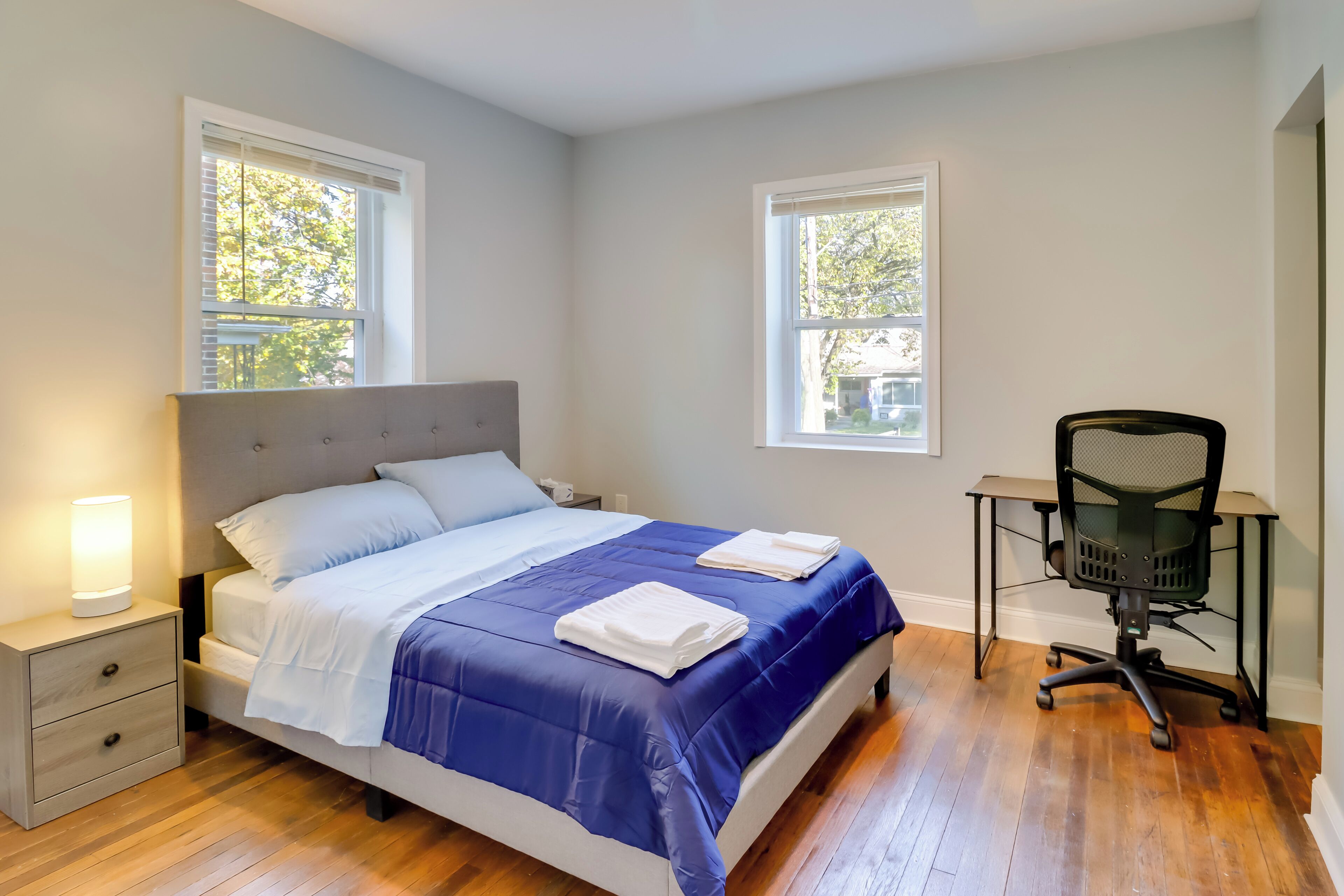 A bedroom with a bed, bedside tables, a desk, and two windows.