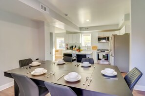 Una cocina moderna con armarios blancos, un refrigerador de acero inoxidable y un comedor con una mesa oscura dispuesta para cuatro personas.