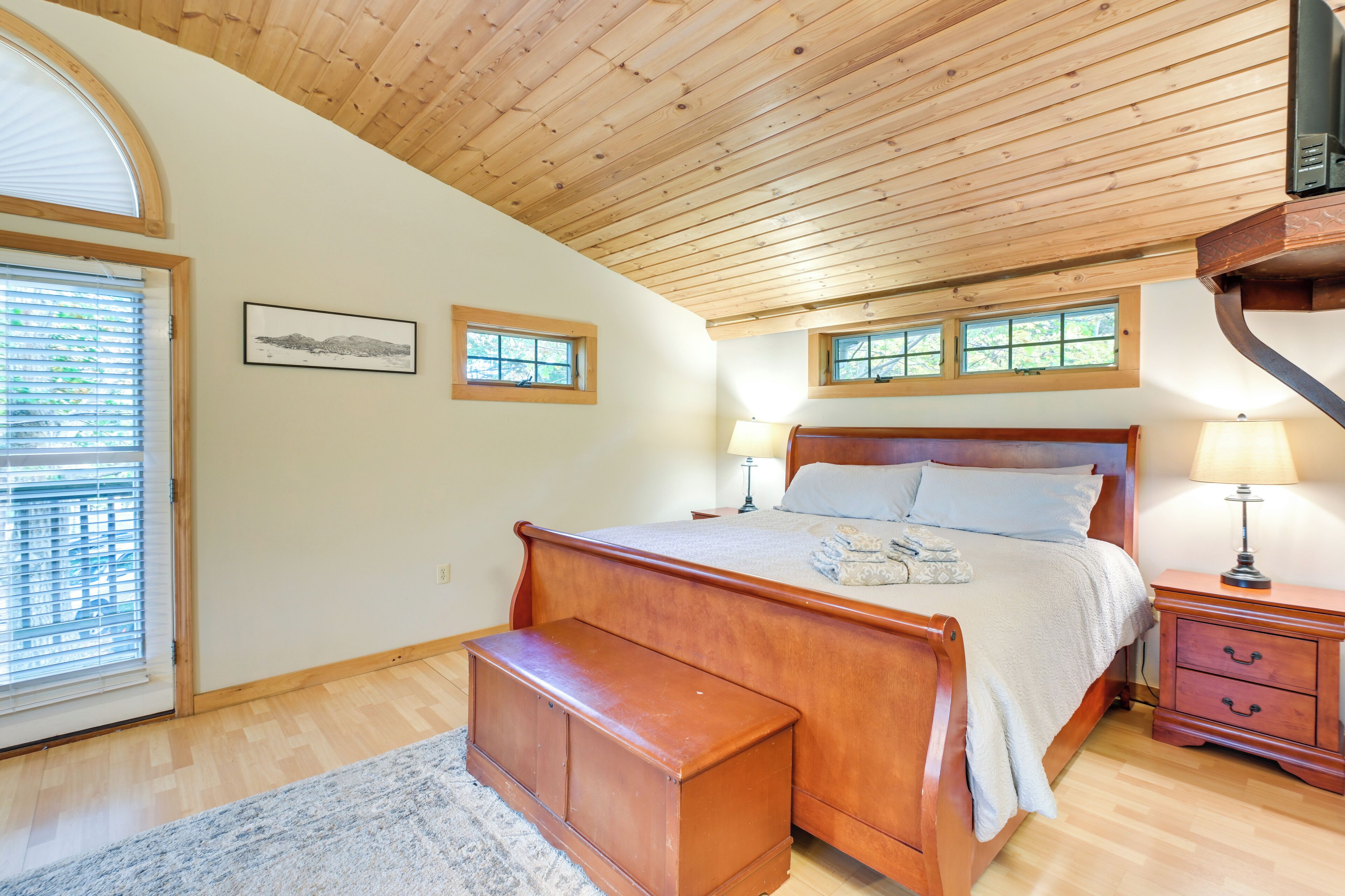 A bedroom with a wooden ceiling, a large bed, a nightstand, and a bench.
