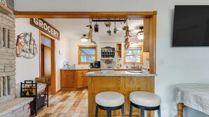 A kitchen with a wooden island, two bar stools, a 'GROCERY' sign, and a stone fireplace. - Antiquing & Fishing: Riverfront Waupaca Home! (Waupaca)