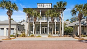 A two-story house with a balcony, surrounded by palm trees.