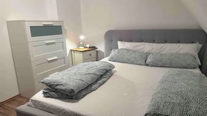 En snyggt bäddad säng med mönstrade filtar, ett sängbord med en lampa och ett arkivskåp.