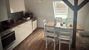 Ett kompakt kök med vita skåp, en inbyggd ugn och en bänkskiva i trä. Ett matbord med vita stolar står placerat nära ett fönster.