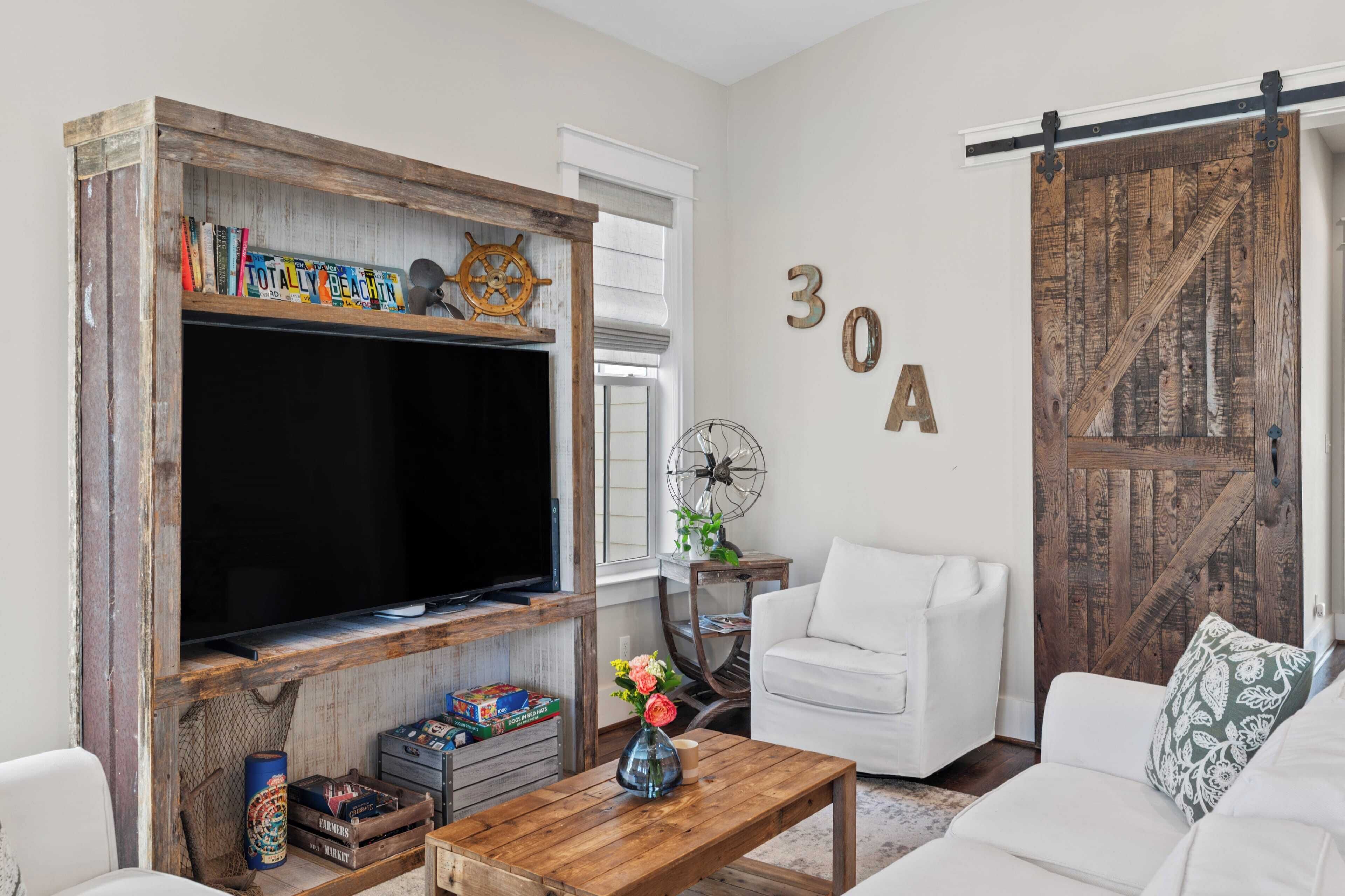 Una sala de estar con televisor, muebles blancos, una mesa de centro de madera y una pared decorativa con el número '30A'.